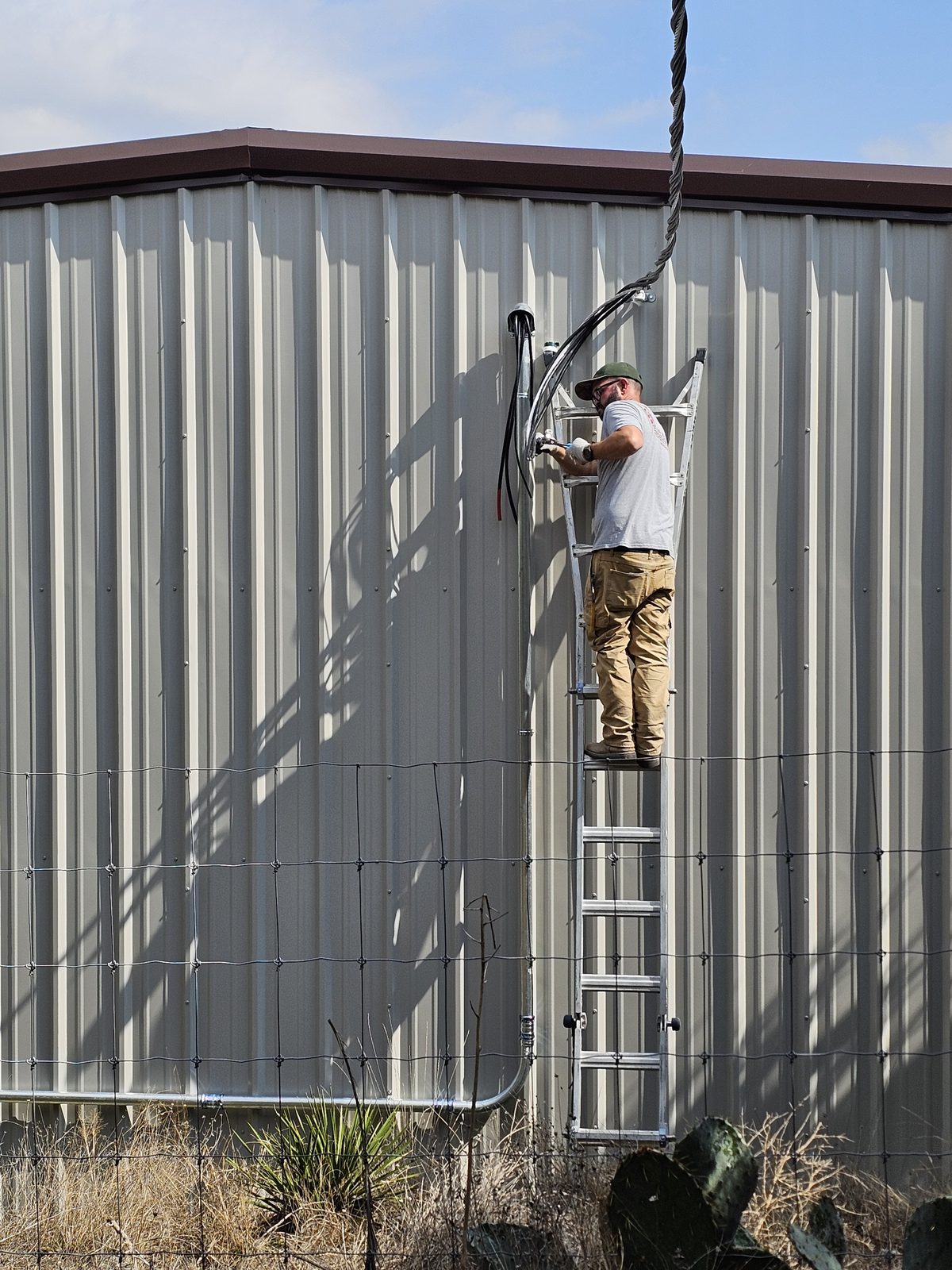 Electrician on a ladder landing a service drop on a metal building