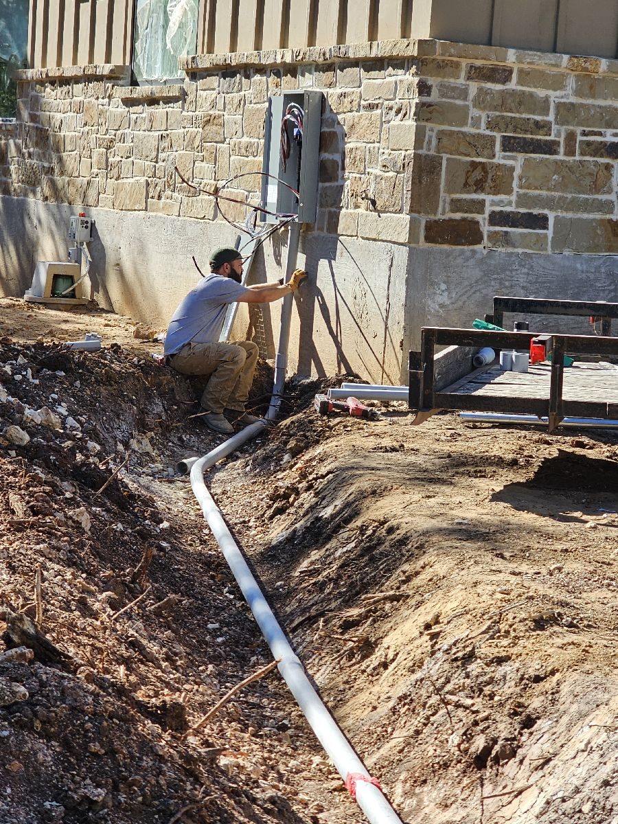 Panel and underground PVC conduit at a stone foundation with an open trench