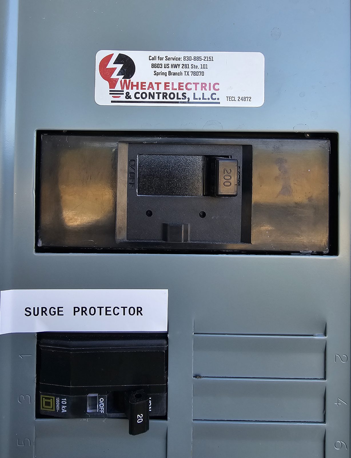 Panel door with a Wheat Electric service sticker and a breaker labeled surge protector